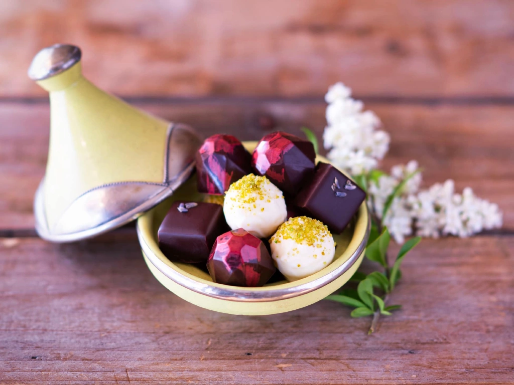 Handgjorda praliner från Criollo chocolaterie, serverade i en liten keramikskål med lock och dekorerade med vita blommor.